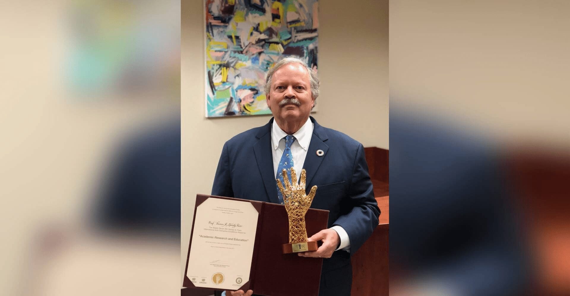 Man in suit holding certificate and trophy